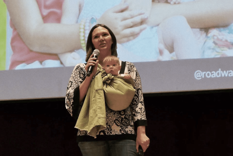 Amber speaking on stage with a baby in a sling.