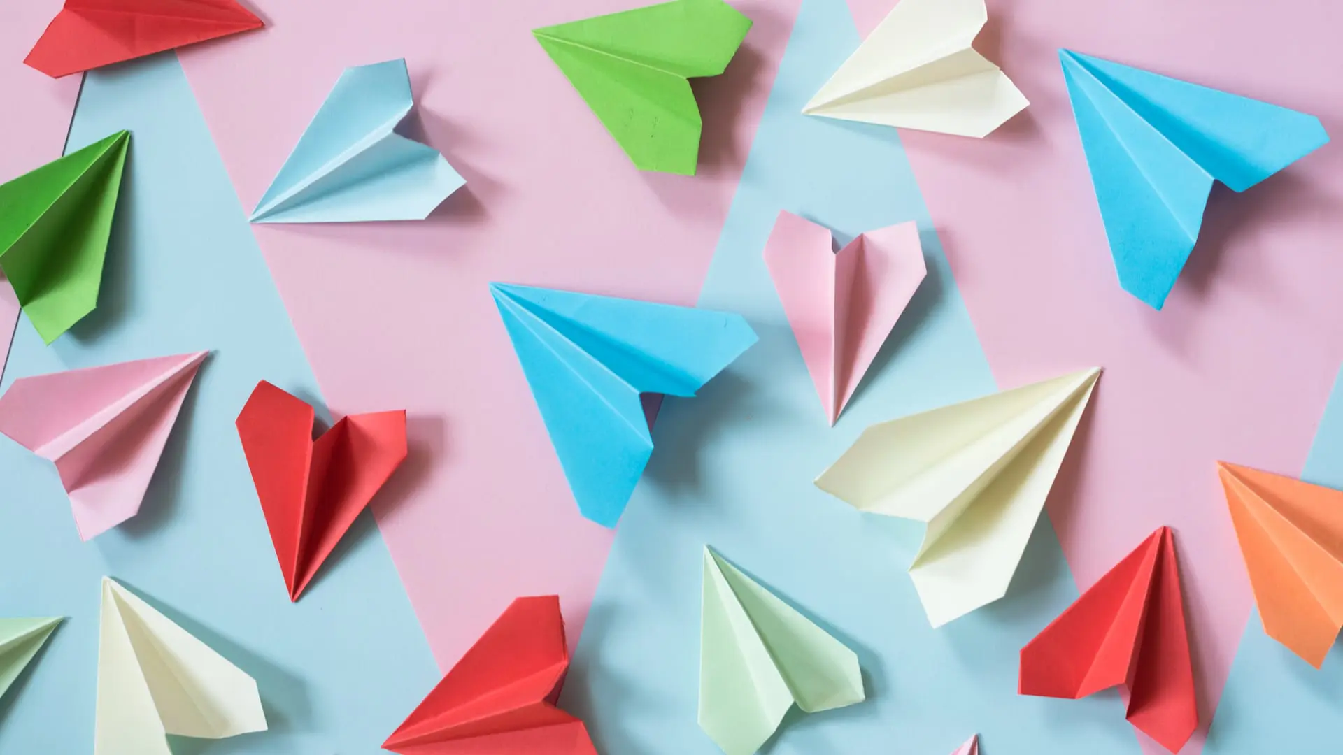 multicolored paper airplane layed out on pink and blue paper