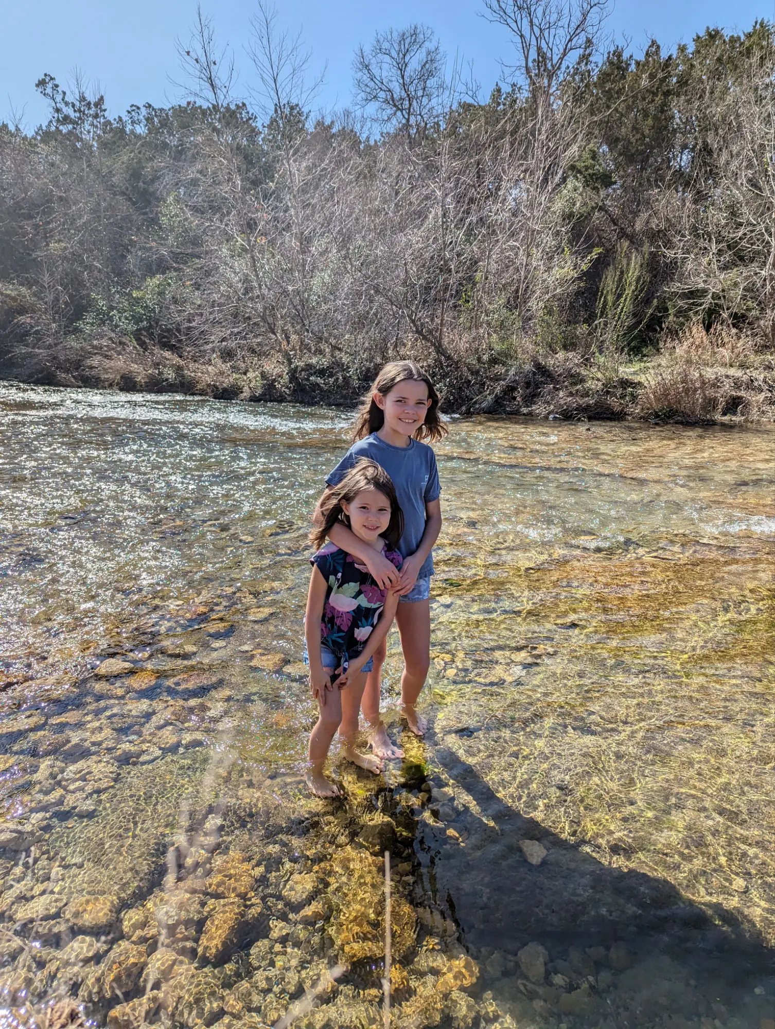 Zara with her arm around Addie as they stand in the river.