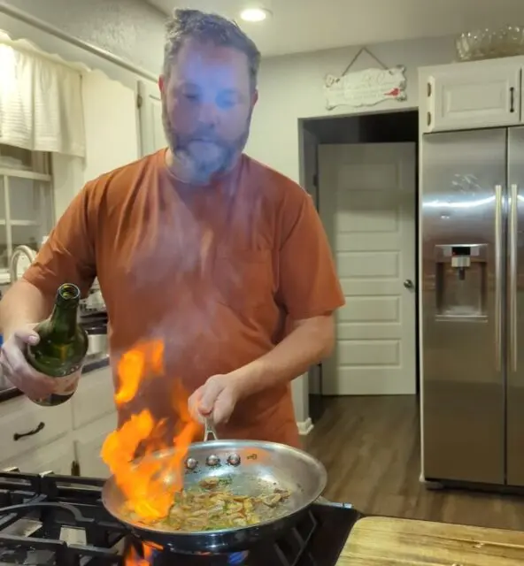 Flames jump from a saute pan with caramelized mushrooms as Chris pours sherry into the pan.