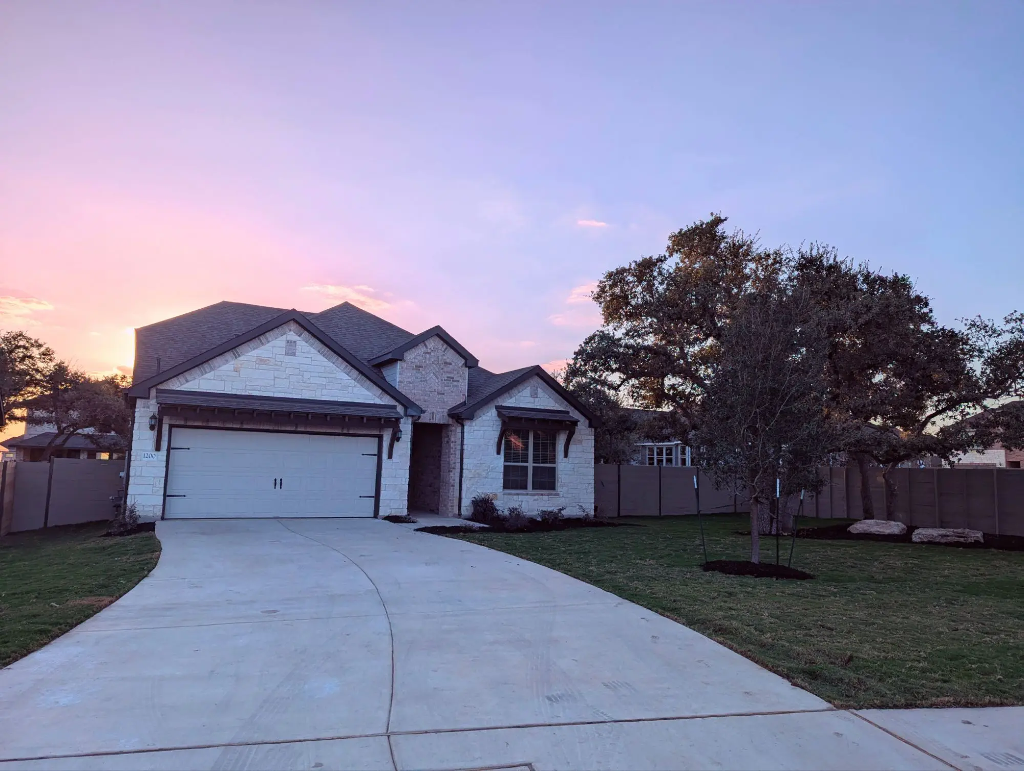 Amber's house has a white stone front with farmhouse-style awnings over the garage door and front window. The house faces east and in this photo, the sun is setting behind it.