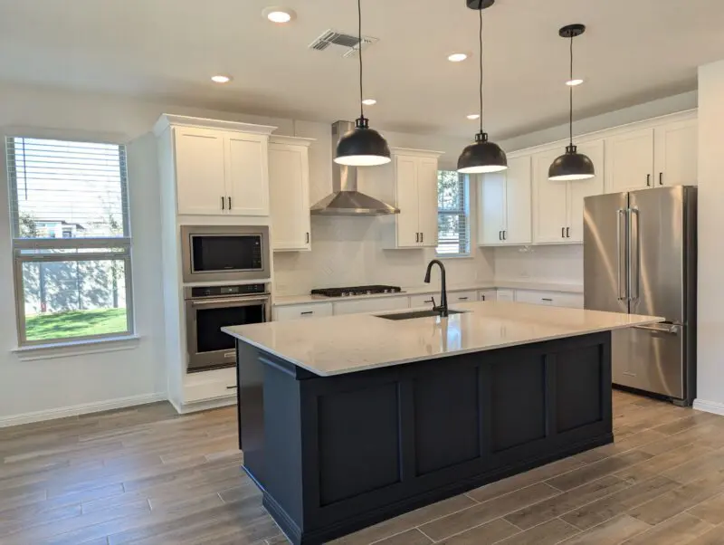 Amber's kitchen has white cabinets and countertops with a black island that has three black pendant lights over it.