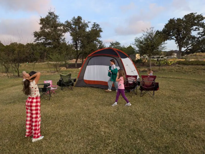 Kids playing statues in the park near a tent.