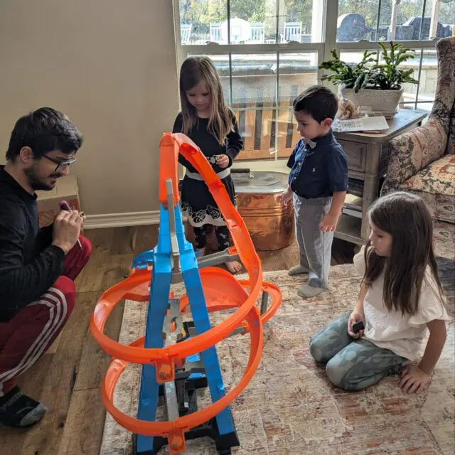 Addie, Vivi, and Romeo play with a hot wheels car track with Uncle Andrei.