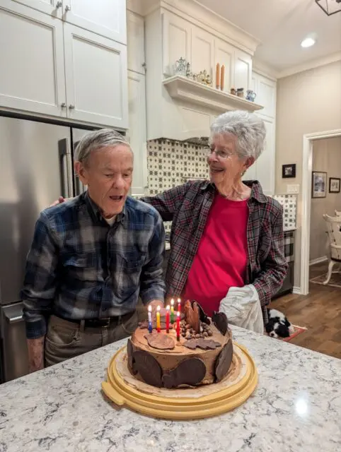 Great Uncle Chuck about to blow out candles on a birthday cake while Great Aunt Sally looks on.