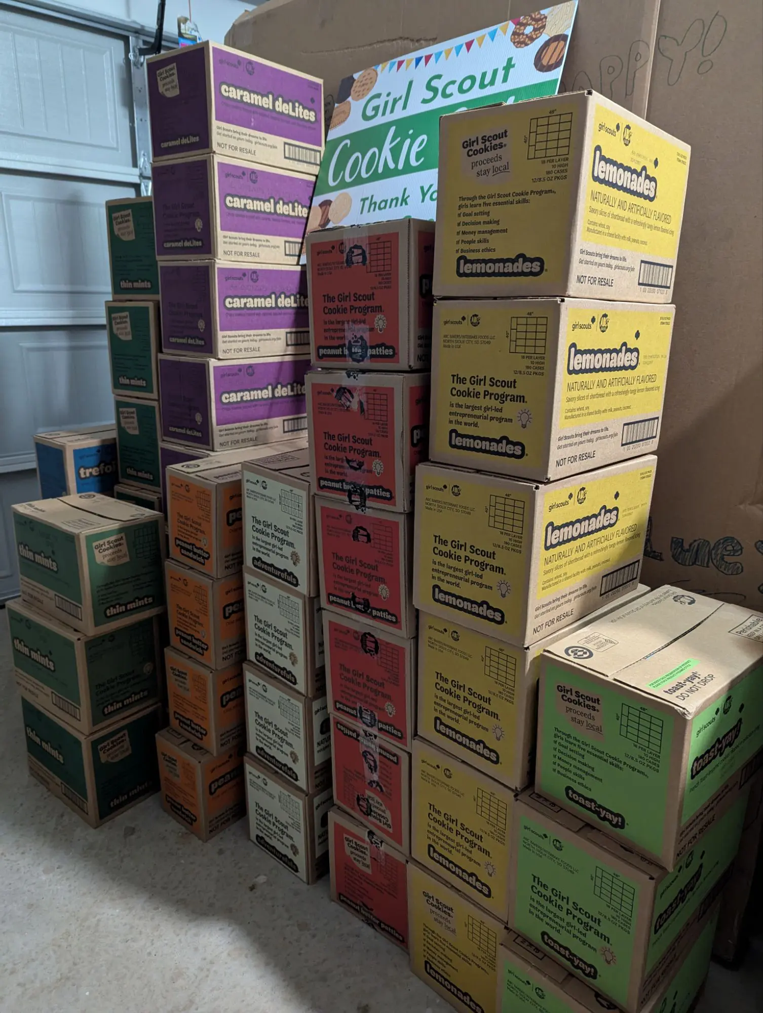 46 cases of Girl Scout cookies stacked by type in a garage.