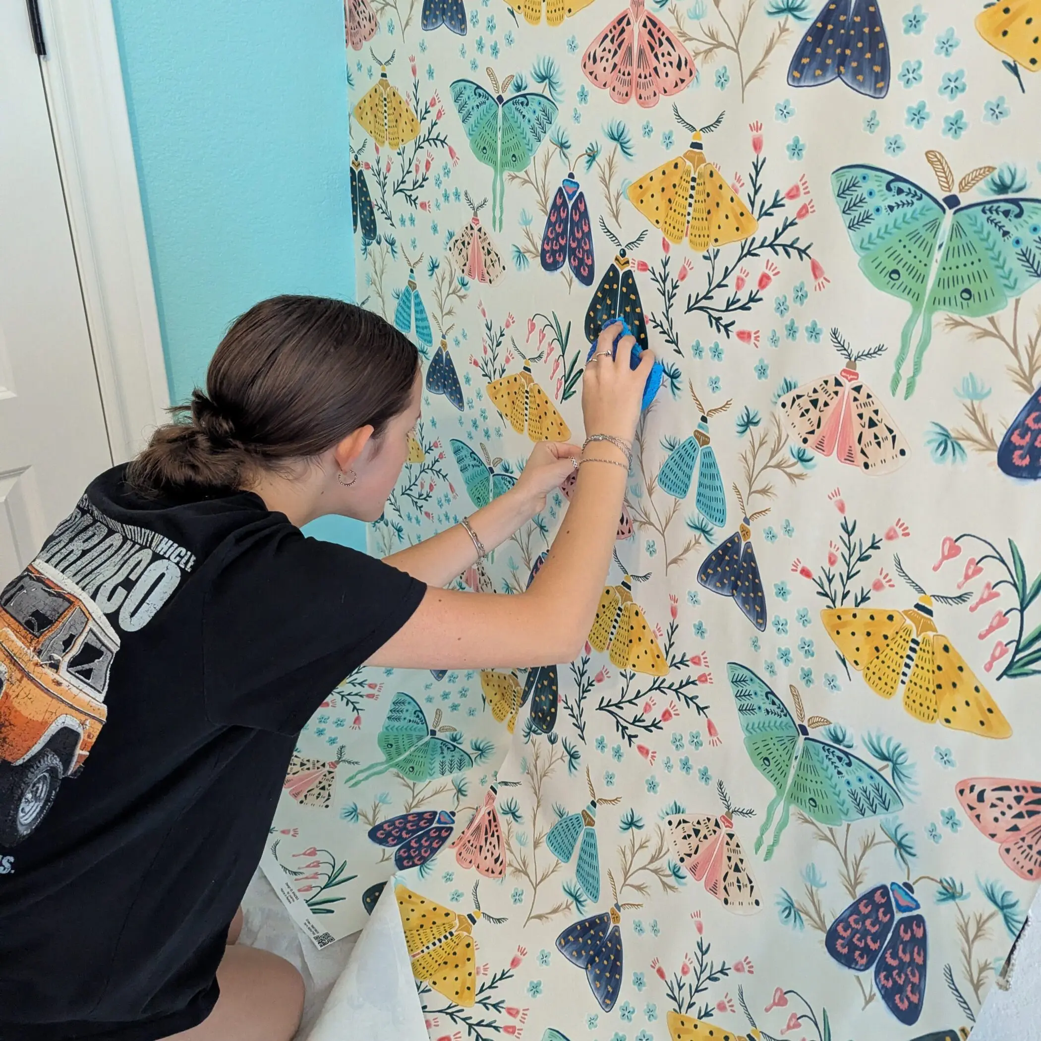 Nora kneeling on the floor lining up wallpaper.