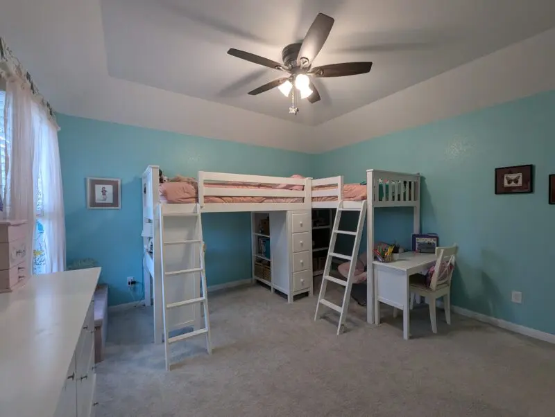 Two white wooden loft beds, each with a desk and storage shelves/drawers put together in an L shape in the back right corner of the room.