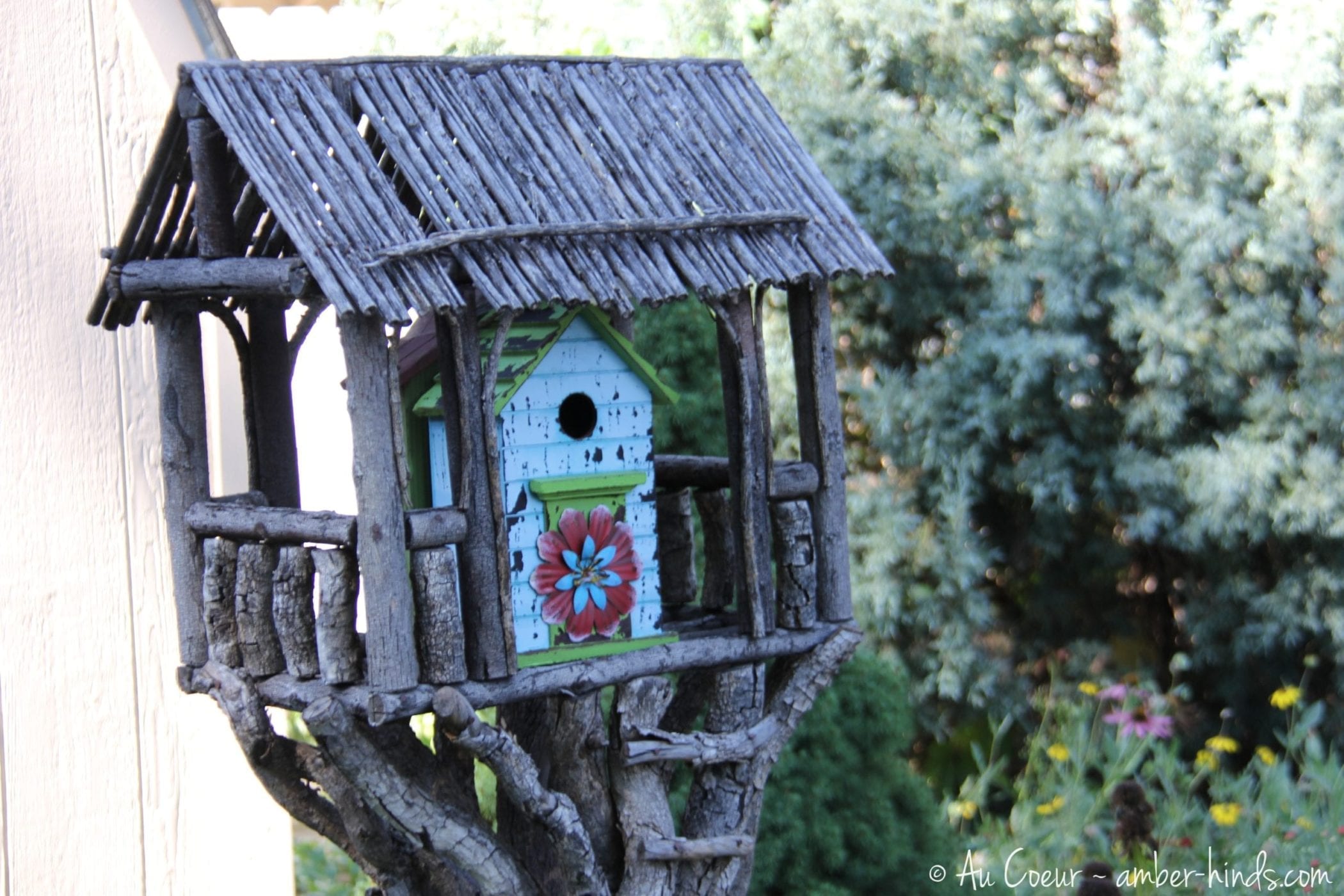 Birdhouse made of sticks and twigs with a tin flower on it.