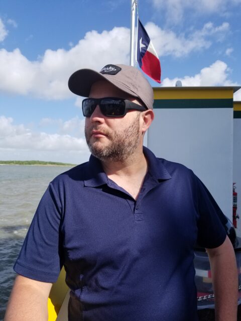Chris riding a ferry boat with a Texas flag behind him.