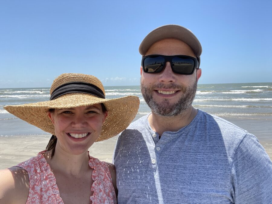 Amber wearing a sun hat and Chris with a baseball cap and sunglasses on a beach