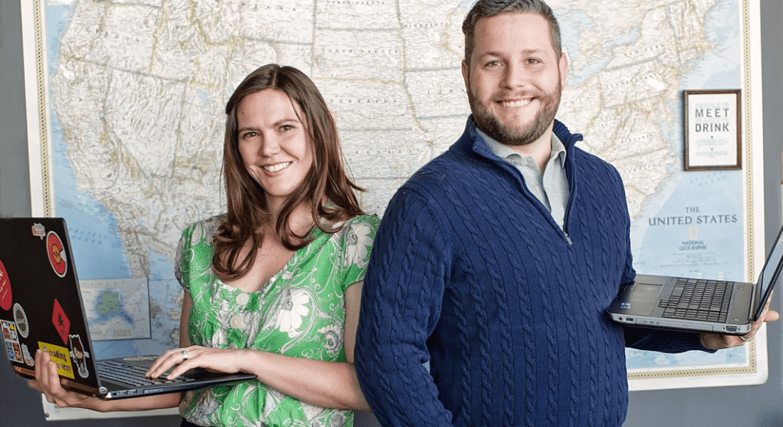 Amber and Chris standing in front of a map and holding their laptops.