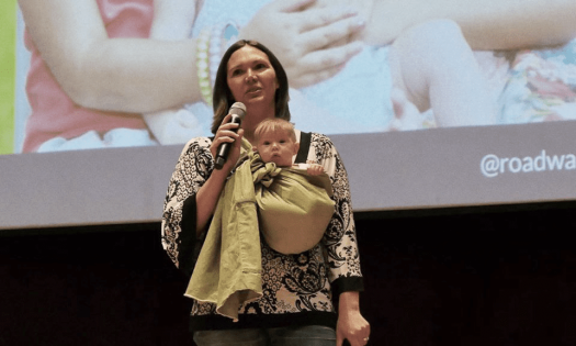 Amber speaking on stage with a baby in a sling