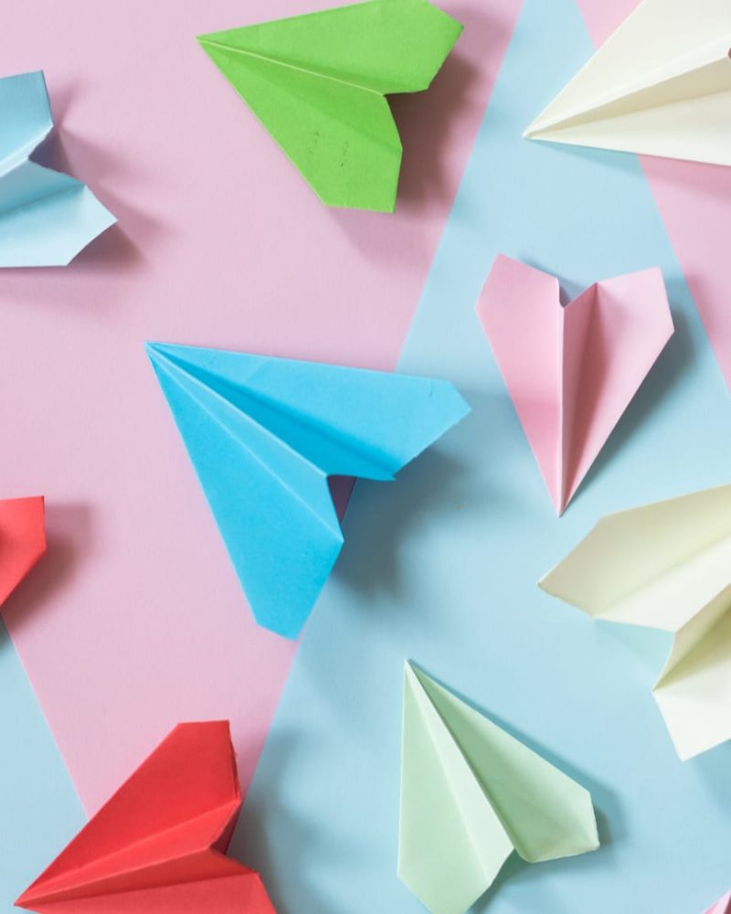 multicolored paper airplane layed out on pink and blue paper